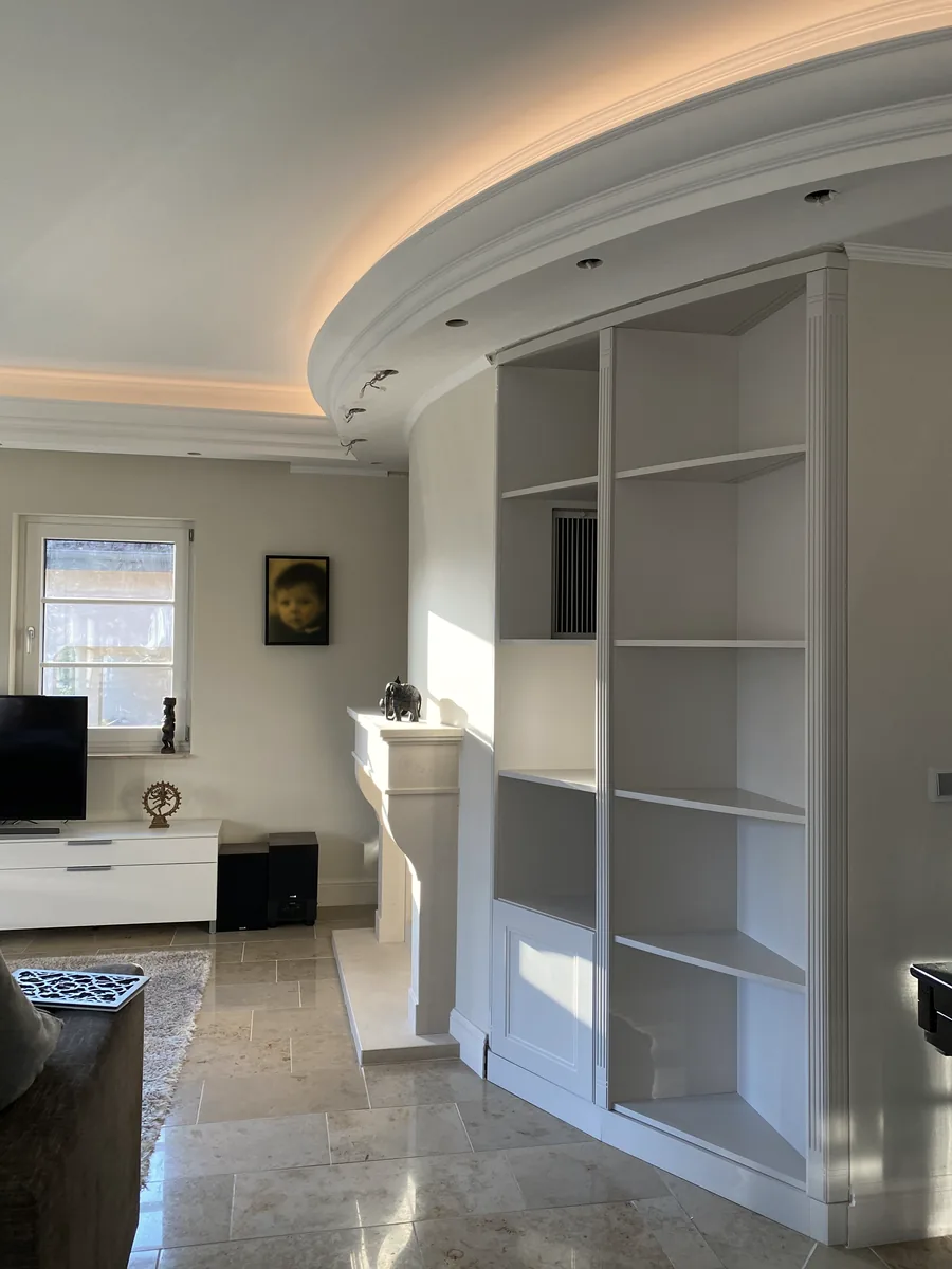 Eckschrank mit Regalen unter der runden Decke, im Vordergrund ein kleiner Teppich und ein dunkler Tisch